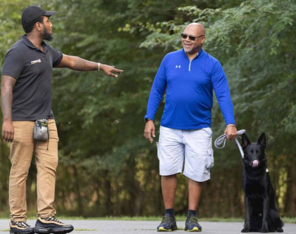 Kenneth Merritt from Merritt Dog Training doing a one on one private lesson with a German shepherd and its two owners. They are walking down a road in a park in Charlotte North Carolina.